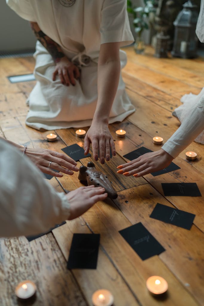 A group of women engaging in a spiritual ritual with candles and cards on a wooden floor indoors.