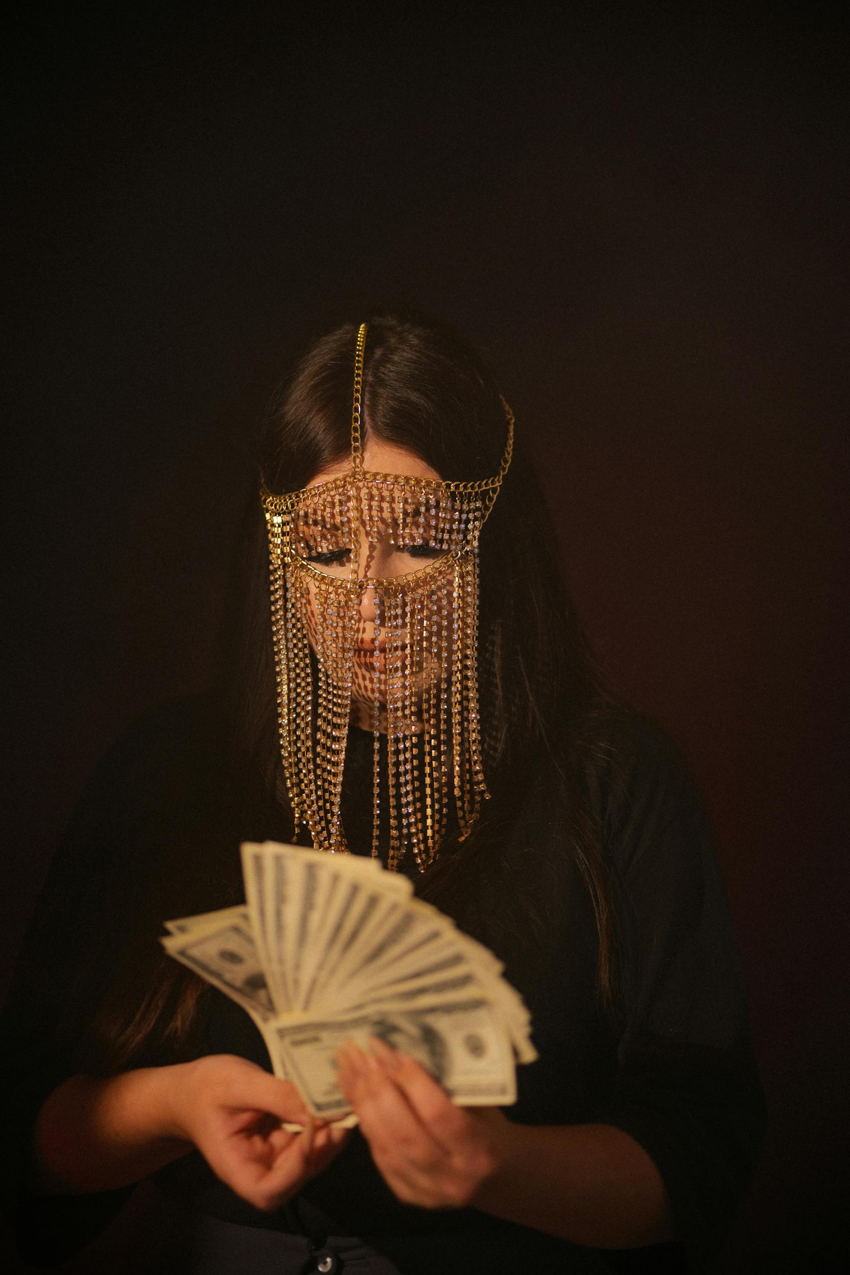 A woman in face chains counts dollar banknotes, symbolizing hidden wealth.