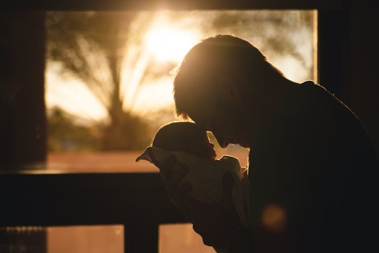 Silhouette of a father holding his newborn at sunset, highlighting love and connection.