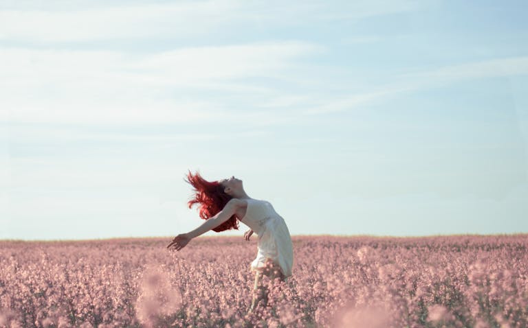 Woman with red hair in a white dress expressing freedom in a vibrant summer field.